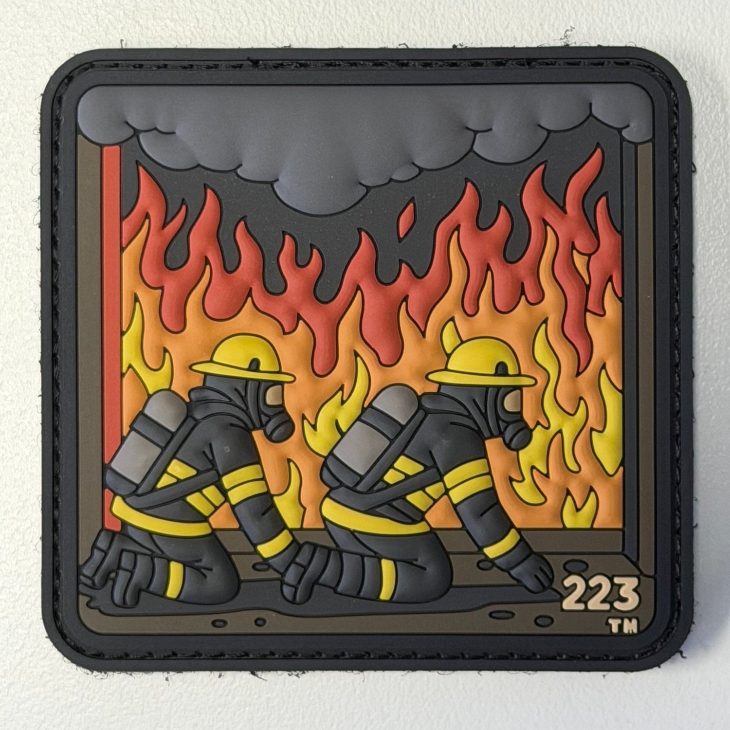 Two firefighters kneeling down with flames and smoke in the background. 